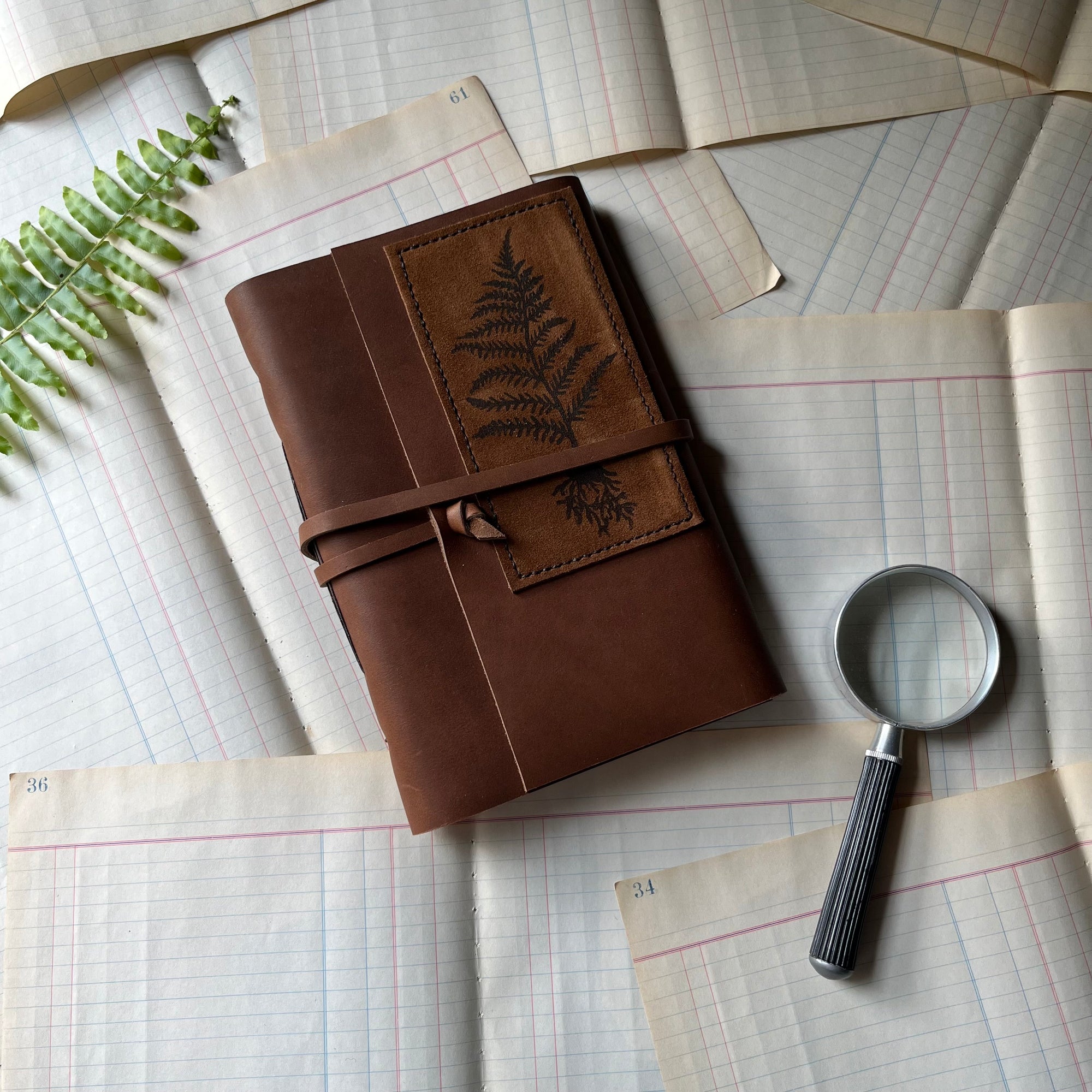 Handmade Leather Journal - guest book, blank journal, nature journal, book journal, gratitude journal - view of the front cover with a stamped fern on suede hand-stitched to the leather cover. A leather thong is attached for tying the journal when not in use.