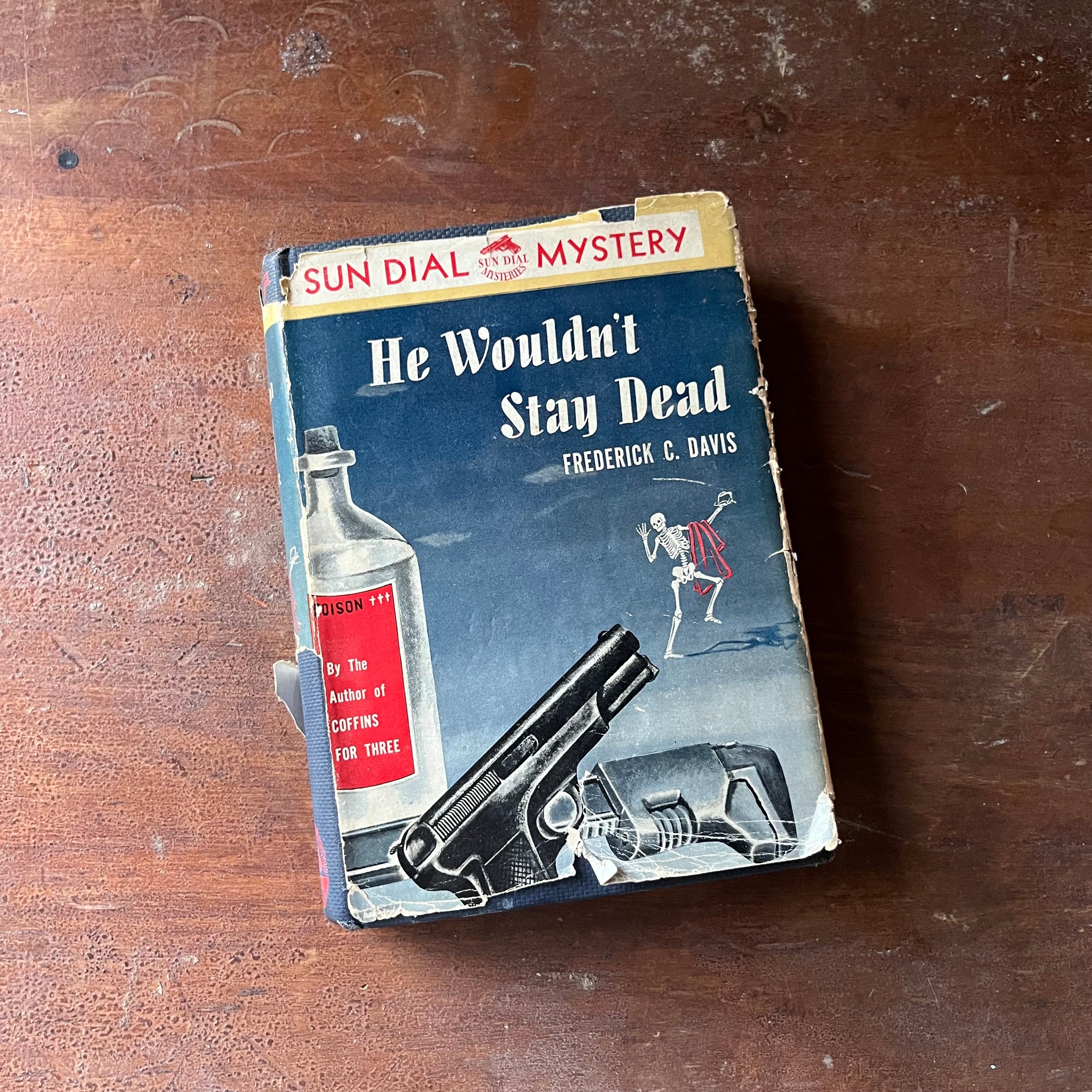 A Sundial Mystery, vintage mystery novel  - He Wouldn't Stay Dead written by Frederick C. Davis - view of the dust jacket's front cover with an illustration of a pistol, a bottle of poison & a dancing skeleton waving