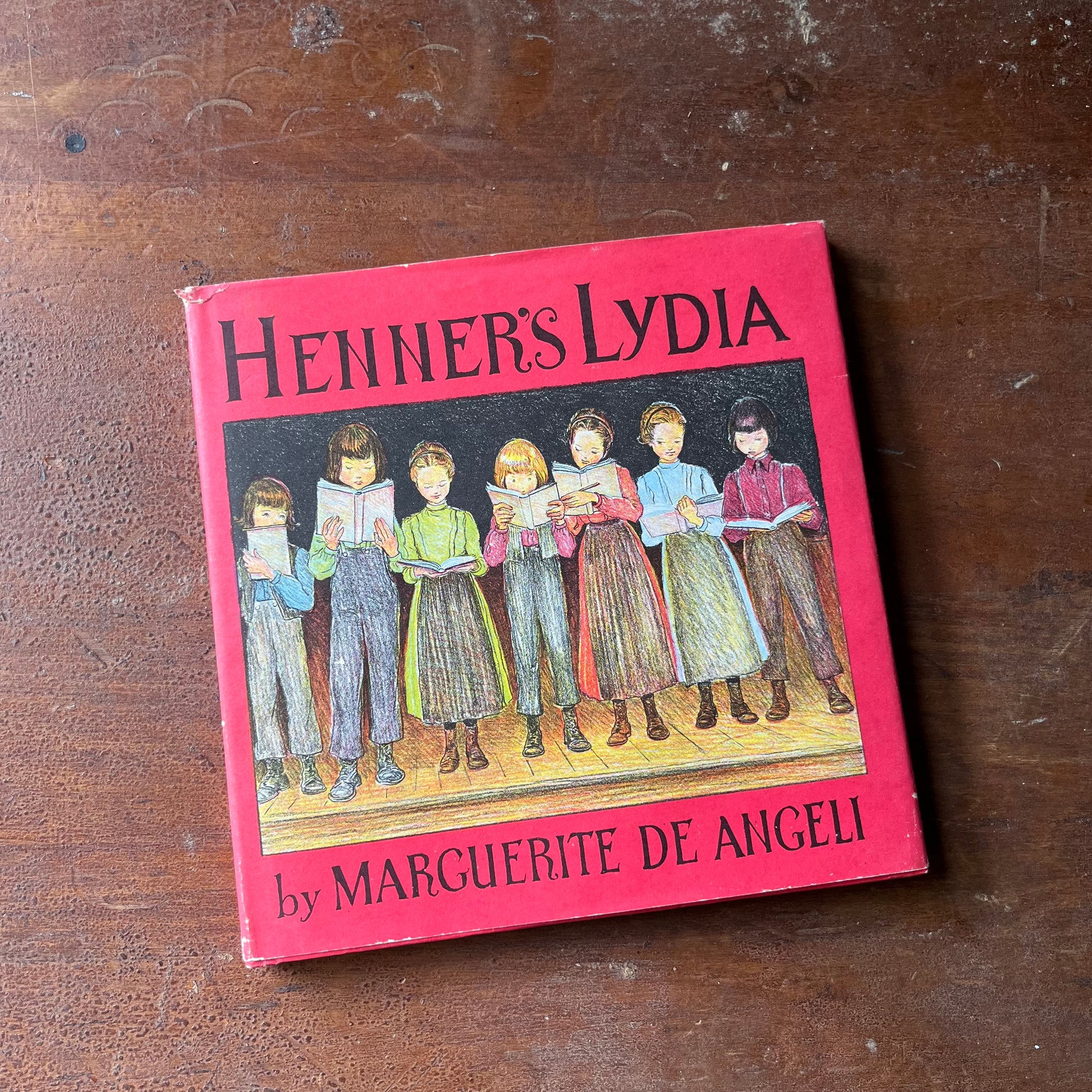 vintage children's chapter book, vintage book about Amish living - Henner's Lydia written and illustrated by Marguerite De Angeli - view of the dust jacket's front cover depicting children lined up in a schoolhouse in front of a blackboard & reading from books
