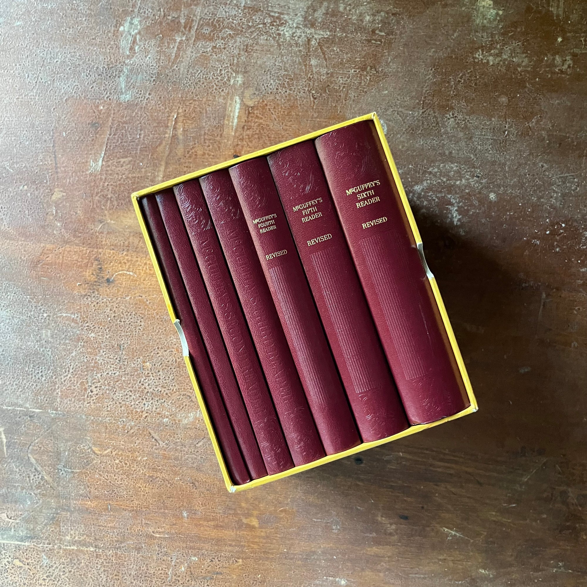 vintage children's books, children's school primers - McGuffey's Eclectic Readers Primer Through the Sixth written by William Holmes McGuffey - Complete Book Set in Cardboard Sleeve - view of the spines - some of which are embossed - rich, maroon color