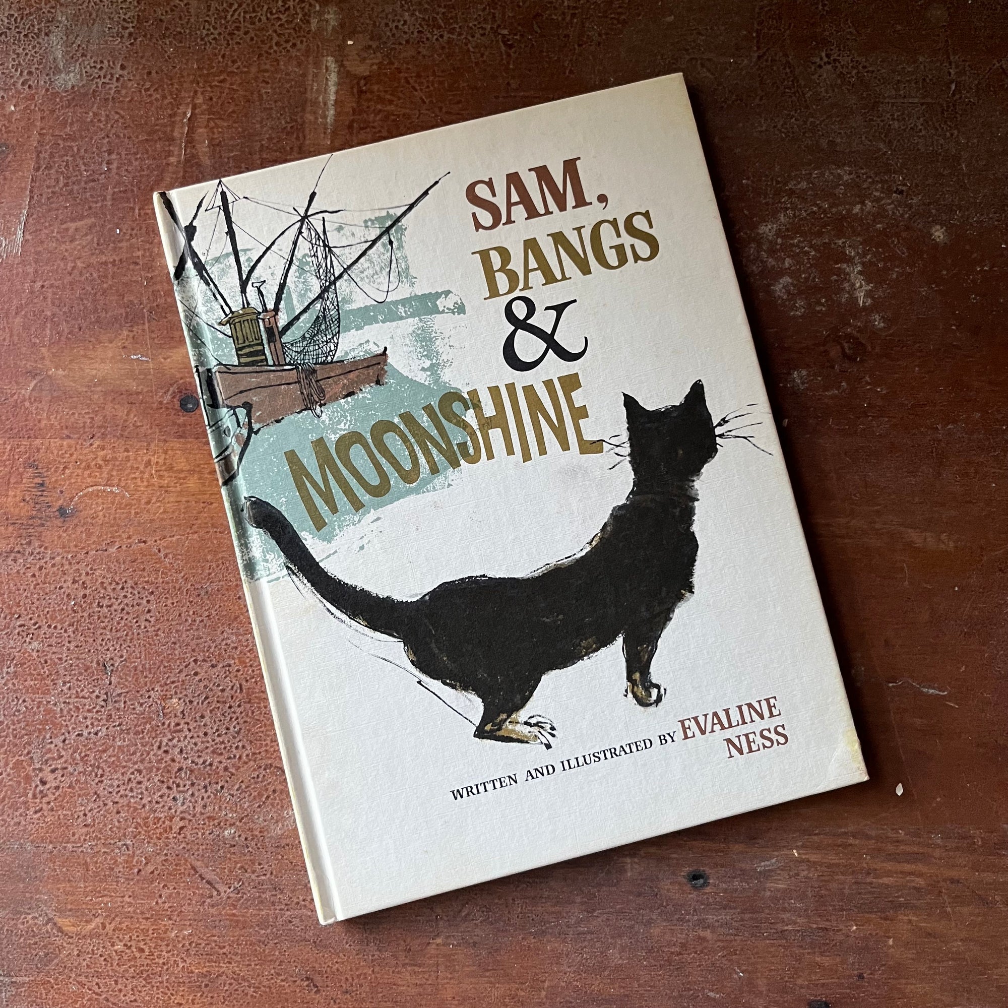 vintage children's picture book, 1967 Caldecott Medal Winner - Sam, Bangs & Moonshine written & illustrated by Evaline Ness - view of the front cover with an illustration of Bangs the cat & a fishing boat in the background
