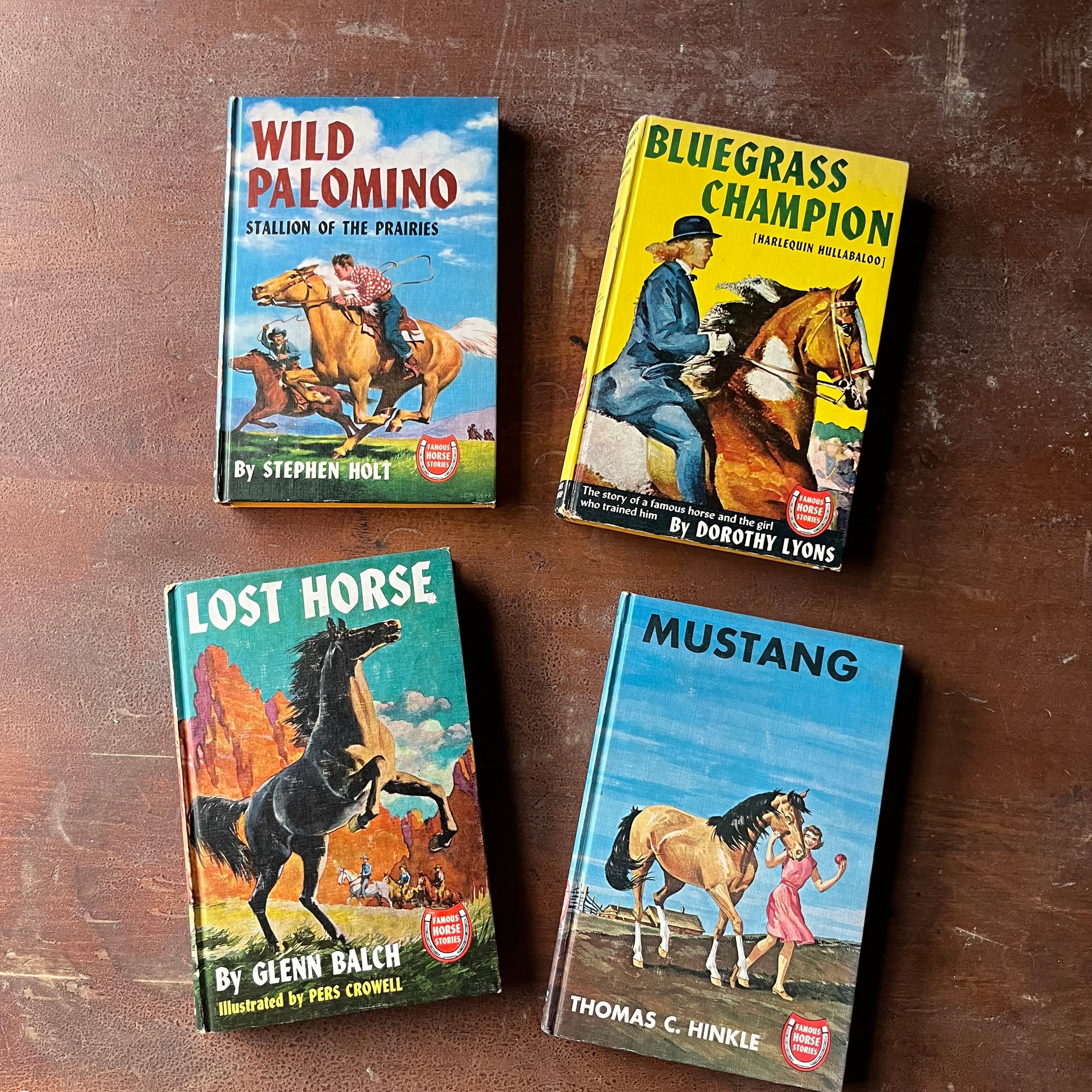 Set of Four Famous Horse Story Books-Mustang, Wild Palomino, Bleugrass Champion & Lost Horse-vintage children's chapter books-view of the colorful front covers in bright blues & yellows all with illustrations of the horse the book features plus the title, author & the Famous Horse Stories Emblem which is red & white with a horseshoe 