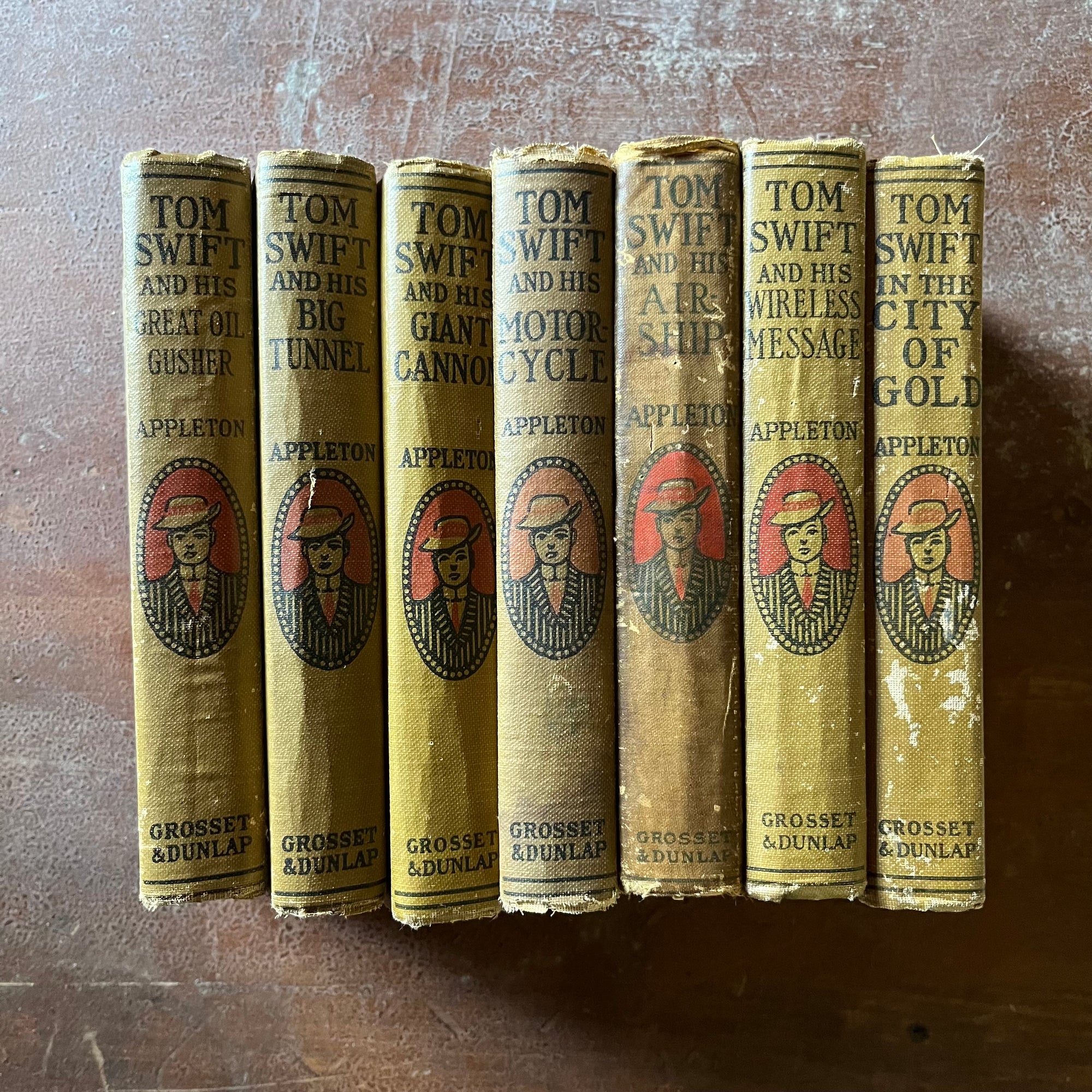 antique children's chapter books, adventure books for boys - Tom Swift Adventure Books Set of 7 written by Victor Appleton - view of the spines with Tom Swift's illustration in the middle with the title & author last name above & publisher below