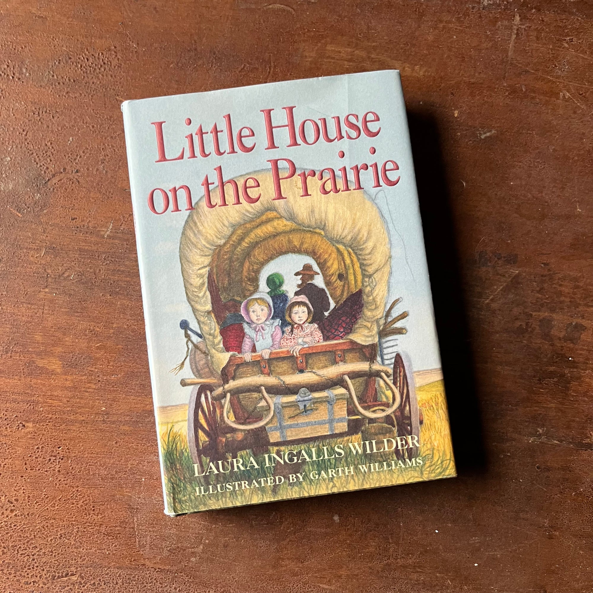 Log Cabin Vintage – vintage children’s book, children’s book, chapter book, living history - Little House on the Prairie 75th Anniversary Edition by Laura Ingalls Wilder with Illustrations by Garth Williams – view of the dust jacket's front cover with the iconic illustration of Luara & Mary sitting in the back of the covered wagon