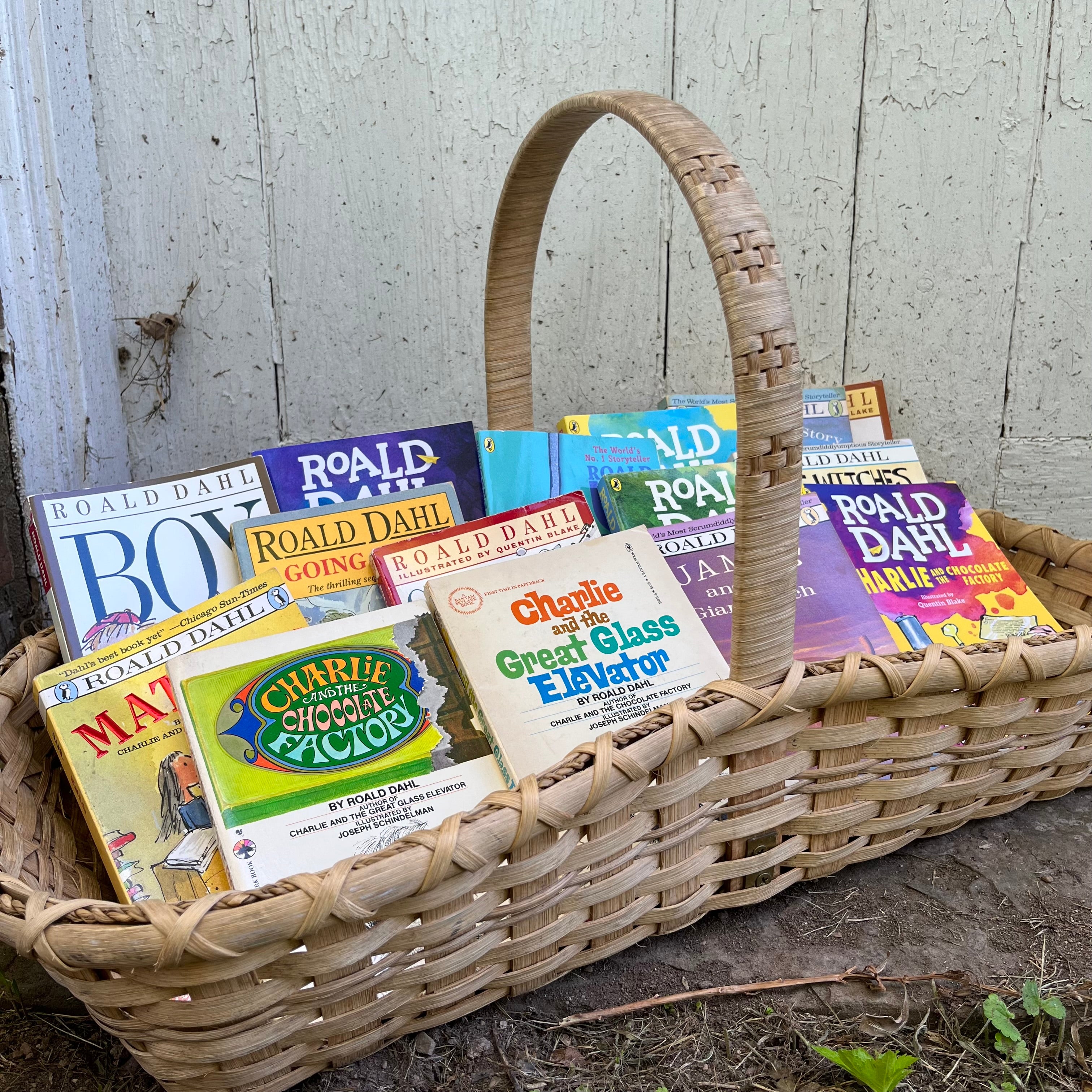 A handmade basket with handle filled with children's books written by Roald Dahl.