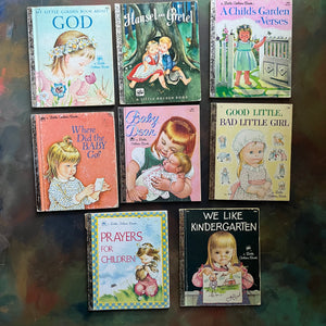 A set of eight vintage Little Golden Books children's picture books arranged in a 3-by-3 grid on a dark, reflective surface. The books feature colorful, classic illustrations and titles including Book about God, Hansel and Gretel, A Child's Garden and Verses, Where Did the Baby Go?, Baby Dear, Good Little, Bad Little Girl, Prayers for Children, and We Like Kindergarten. View of the front covers.