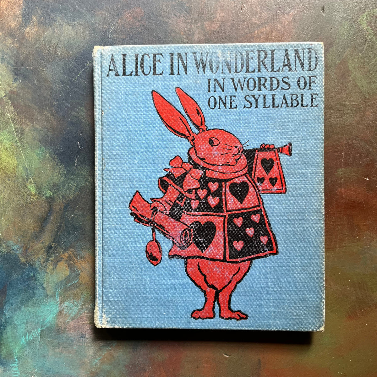 Alice in Wonderland in Words of One Syllable by Lewis Carroll-John Tenniel illustrations-antique Alice in Wonderland book-children's chapter book-living book-view of the embossed front cover with the white rabbit in red & black
