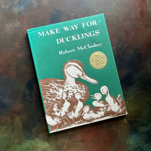 Make Way for Ducklings-Robert McCloskey-Caldecott Winning Picture Book-vintage children's picture book-must read children's book-Log Cabin Vintage Top 100 Must Read Children's Book-view of the dust jacket's front cover with Mrs. Mallard and her ducklings pictured along with a gold-colored Caldecott Medal Sticker shown