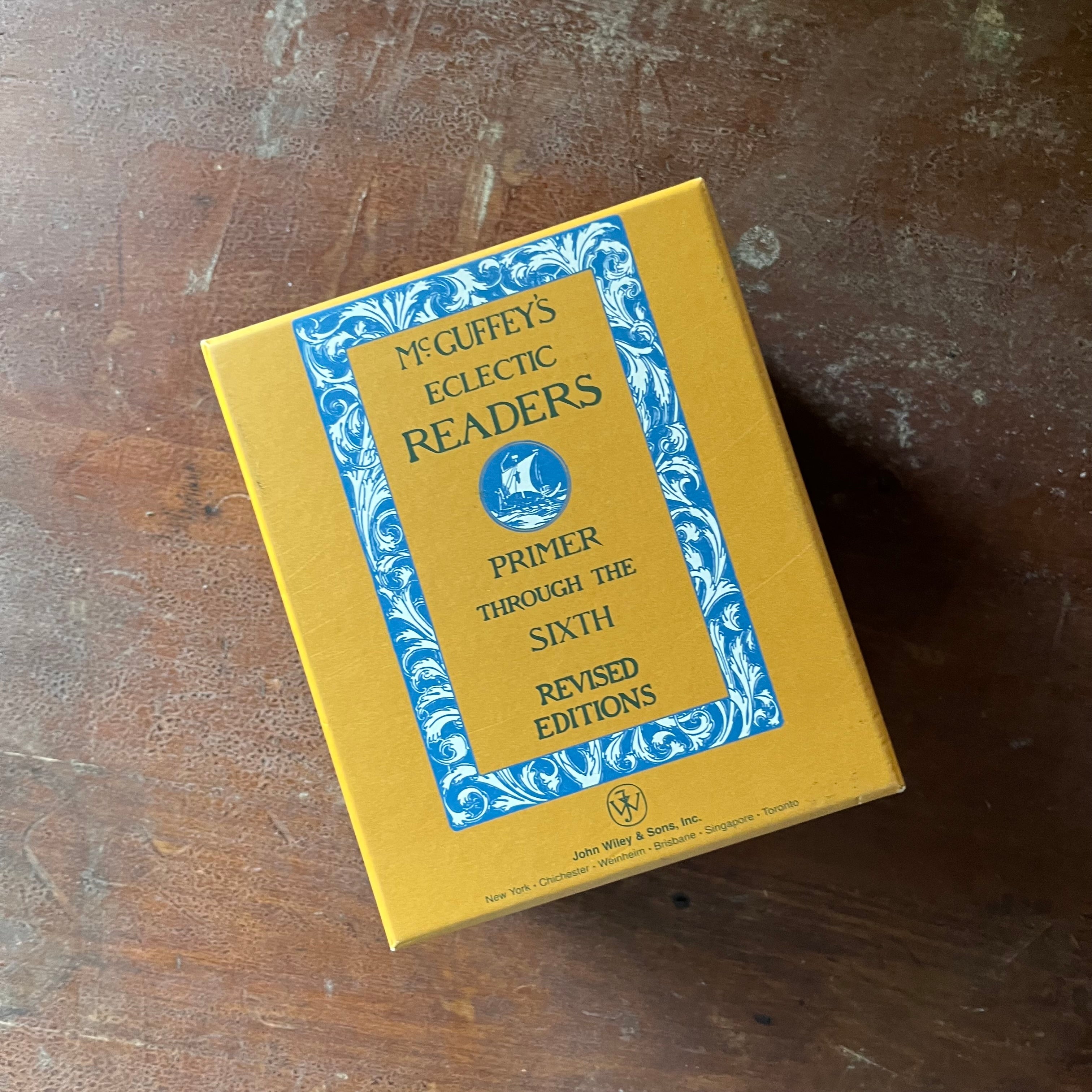 vintage children's books, children's school primers - McGuffey's Eclectic Readers Primer Through the Sixth written by William Holmes McGuffey - Complete Book Set in Cardboard Sleeve - view of the side of the book sleeve - it is yellow with a blue and white design & blue writing listing the set
