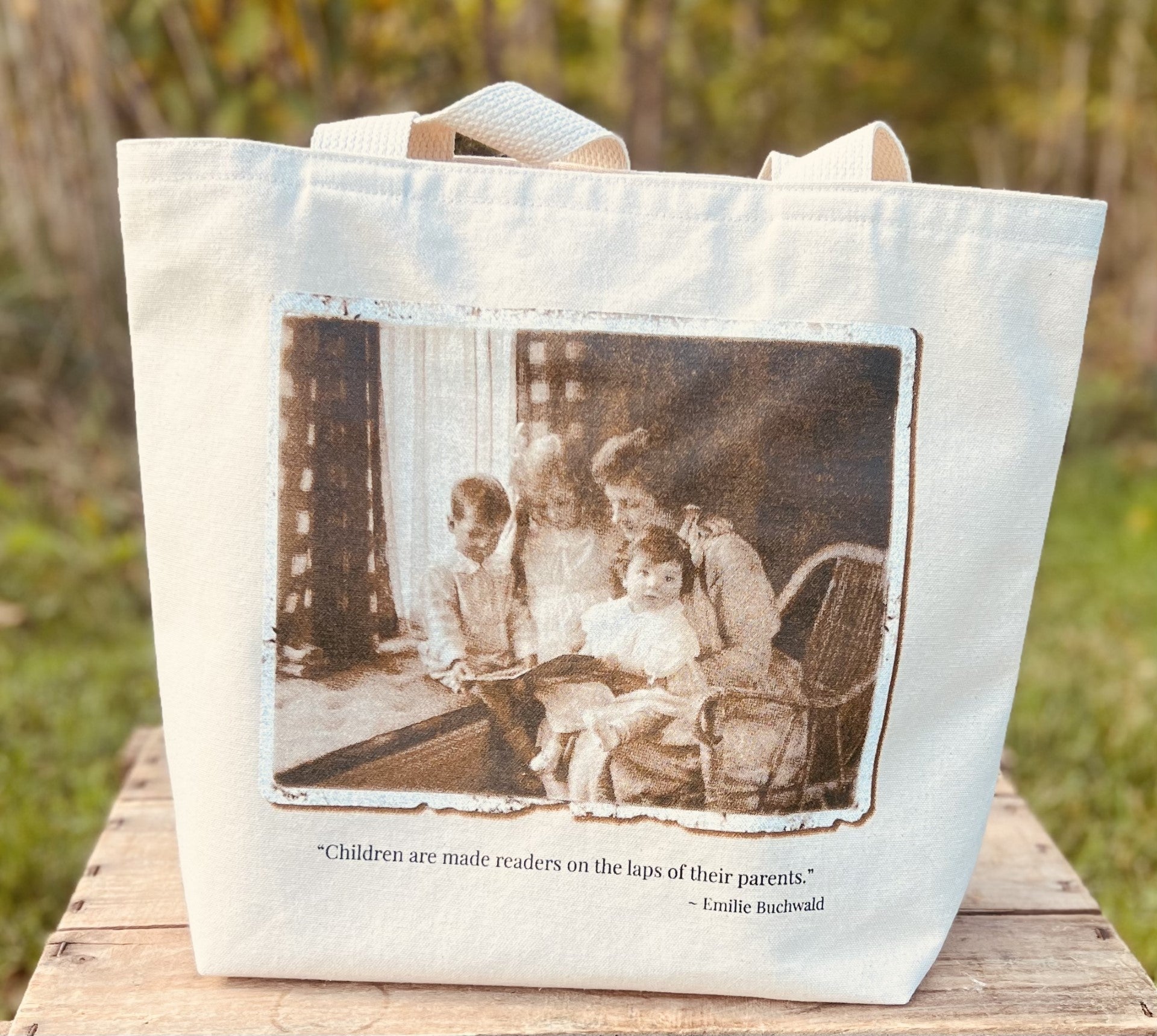 Log Cabin Vintage-canvas book tote bag-view of the front of the bag with a screenprint of an old photograph of a mother reading to three children - lifestyle shot of the bag outside
