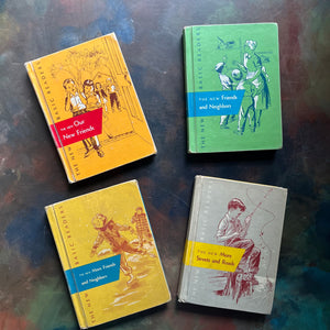 Four vintage hardcover children's books arranged on a dark textured surface. The books include 'The Old Our New Friends' in orange with a red band, 'The New Friends and Neighbors' in green with a blue band, 'The New More Friends and Neighbors' in yellow with a blue band, and 'The New More Streets and Roads' in gray with a yellow band. New Basic Readers published by Scott, Foresman and Company Publishers as part of the Curriculum Foundation Series. 