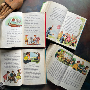 New Basic Readers published by Scott, Foresman and Company Publishers as part of the Curriculum Foundation Series. Four vintage children's schoolbooks arranged in a flat-lay on a dark textured surface showing the illustrations within the pages of these vintage readers.