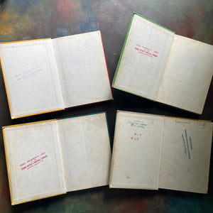 New Basic Readers published by Scott, Foresman and Company Publishers as part of the Curriculum Foundation Series. Four vintage hardcover books shown open, arranged in a 2x2 grid on a dark, textured surface. The pages are aged and cream-colored, with some red and green printed text and markings visible on the inner covers. school stamps noted on these inside covers.