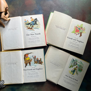 New Basic Readers published by Scott, Foresman and Company Publishers as part of the Curriculum Foundation Series. Four vintage children's books arranged on a dark tabletop, with two books open to show illustrated covers and two books showing open pages. A wooden hand doll is partially visible at the top left.