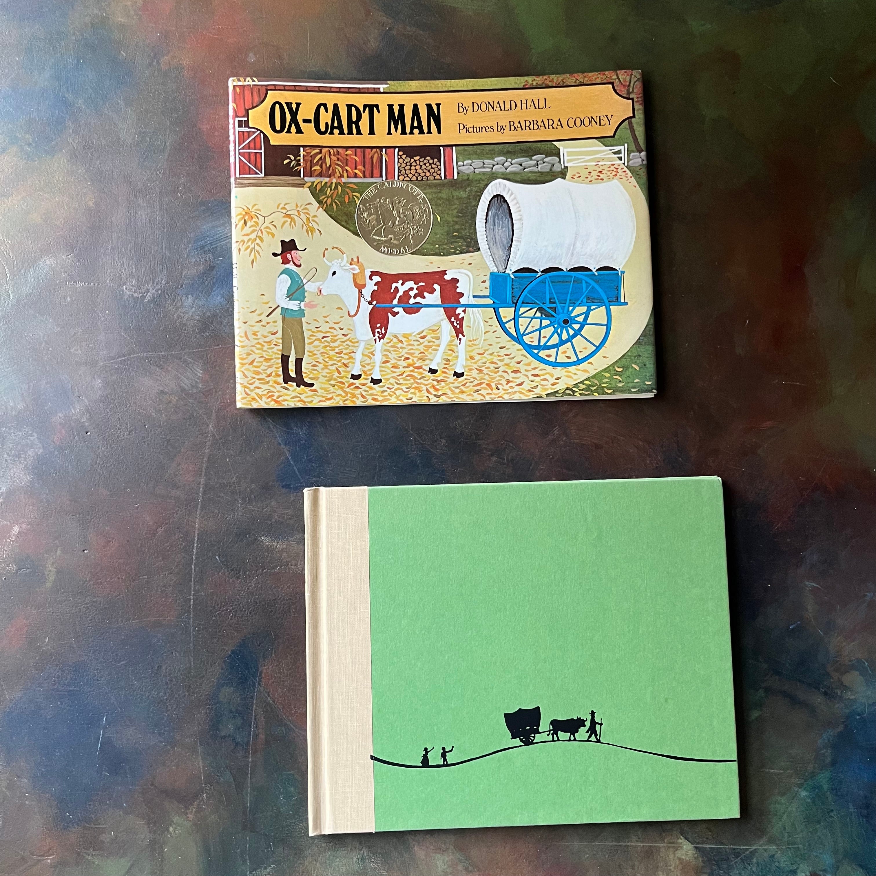 Ox-Cart Man written by Donald Hall with illustrations by Barbara Cooney-vintage children's picture book-1980 Caldecott Medal Winner-view of the front cover in green with an image of a man leading an ox and cart with children following behind.