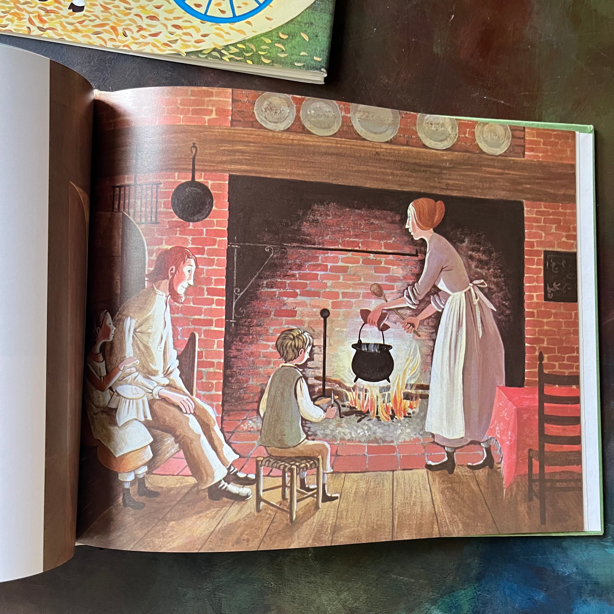 Ox-Cart Man written by Donald Hall with illustrations by Barbara Cooney-vintage children's picture book-1980 Caldecott Medal Winner-view of an illustration of the family sitting around the hearth with a pot of soup or stew being booked over the open fire.