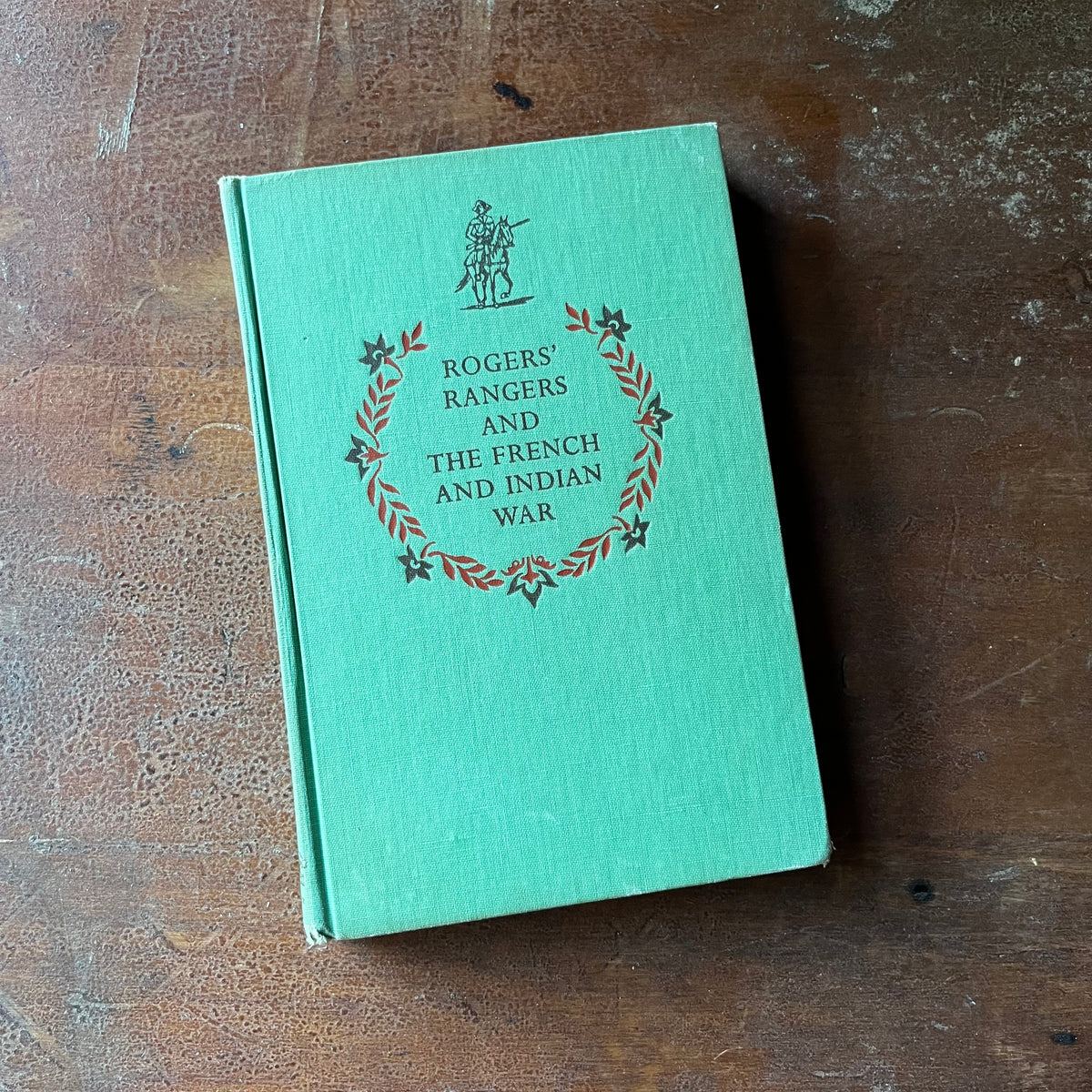 vintage children's living history book - Rogers' Rangers and The French and Indian War written by Bradford Smith with illustrations by John C. Wonsetler - view of the embossed front cover - green with a soldier on horseback along with the title embossed under the illustration - the wreath surrounds the title - the wreath is found on all early Landmark Series books