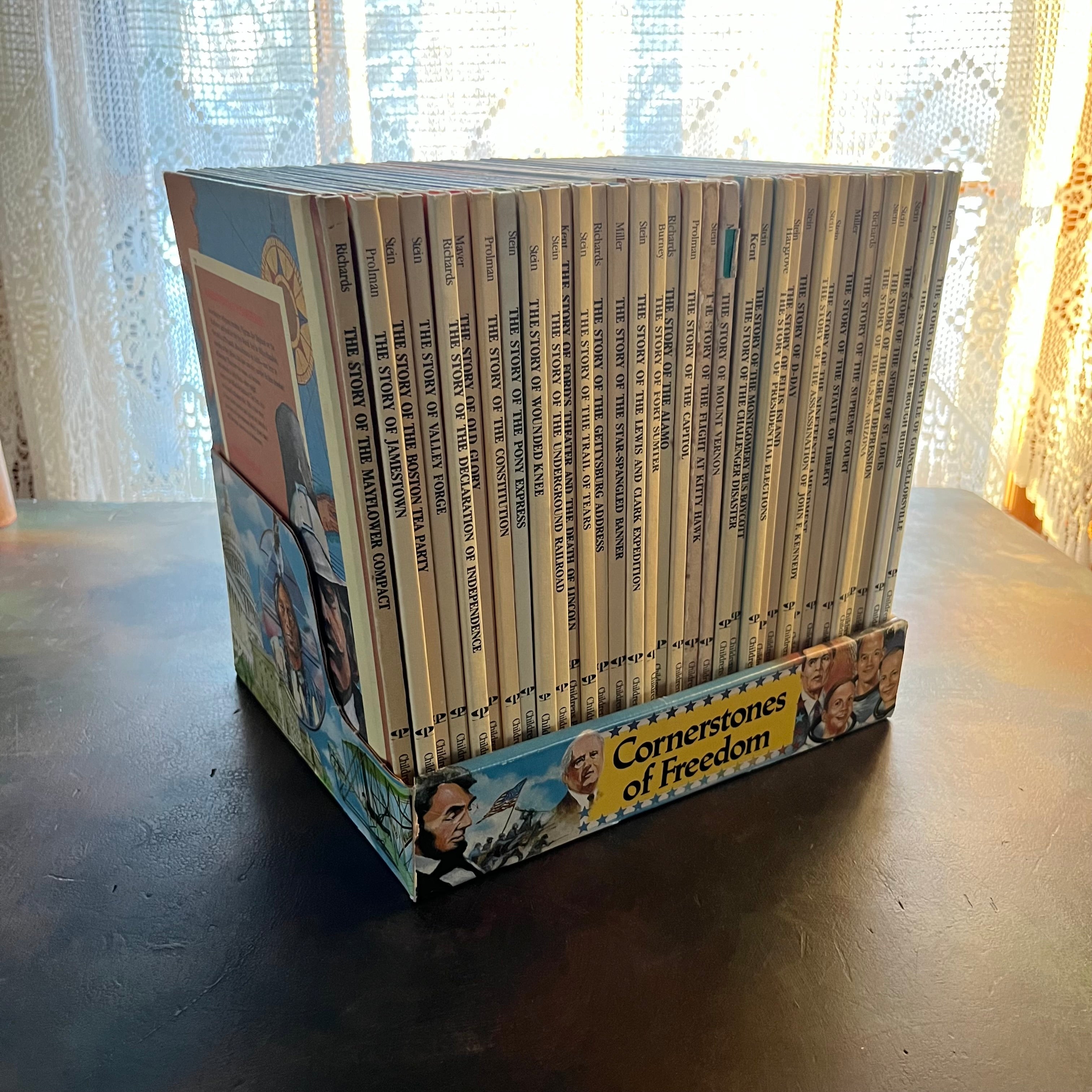 Set of 34 Cornerstones of Freedom History Books for Children in cardboard sleeve holder-vintage US History Picture Books-Early Readers-America250-view of the spines sitting inside the cardboard sleeve holder.