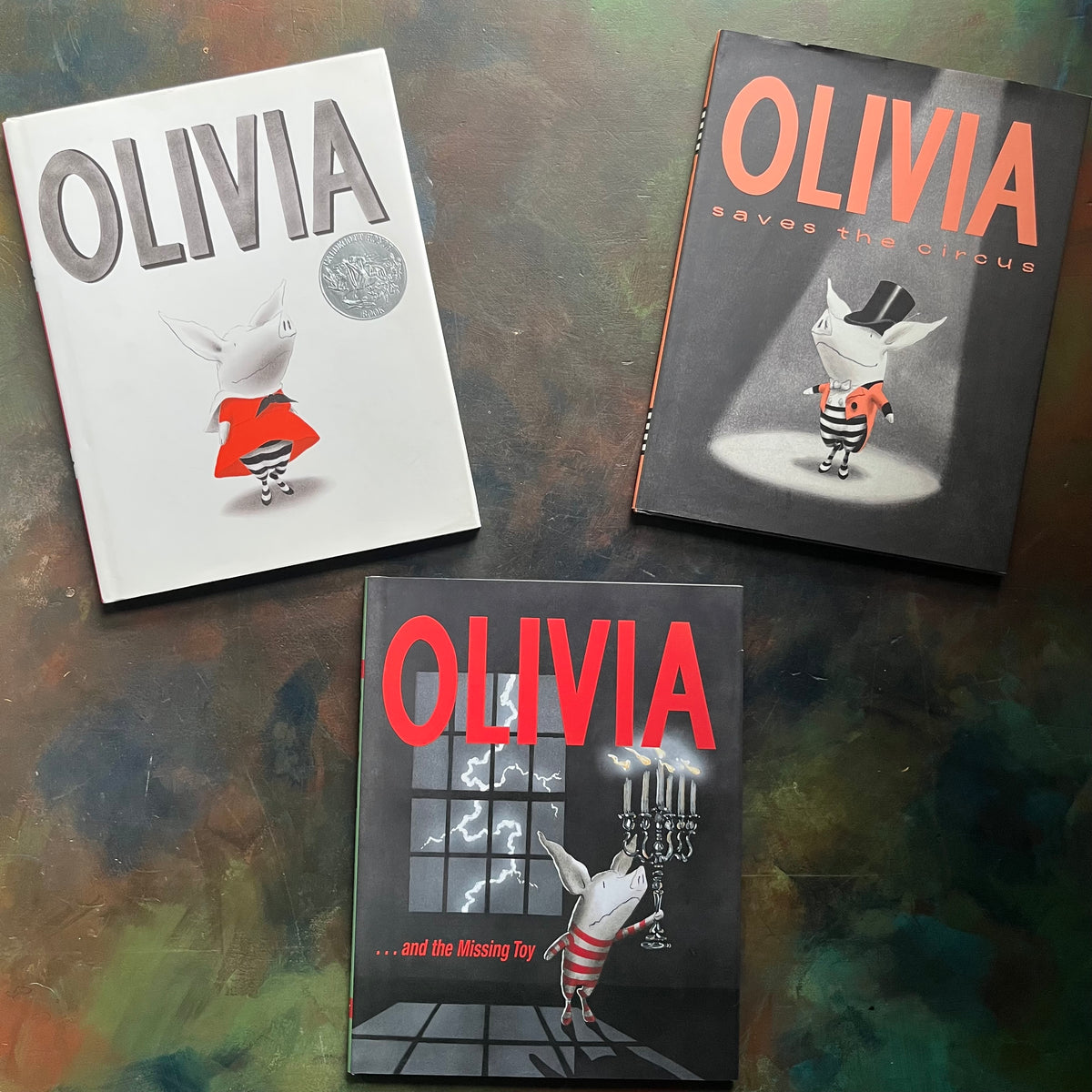 Set of Three Olivia Books written and illustrated by Ian Falconer-Olivia-Olivia Saves the Circus-Olivia and the Missing Toy-award-winning picture book-Caldecott Honor Book-view of the dust jacket's front covers with images of Olivia the Pig on each one.