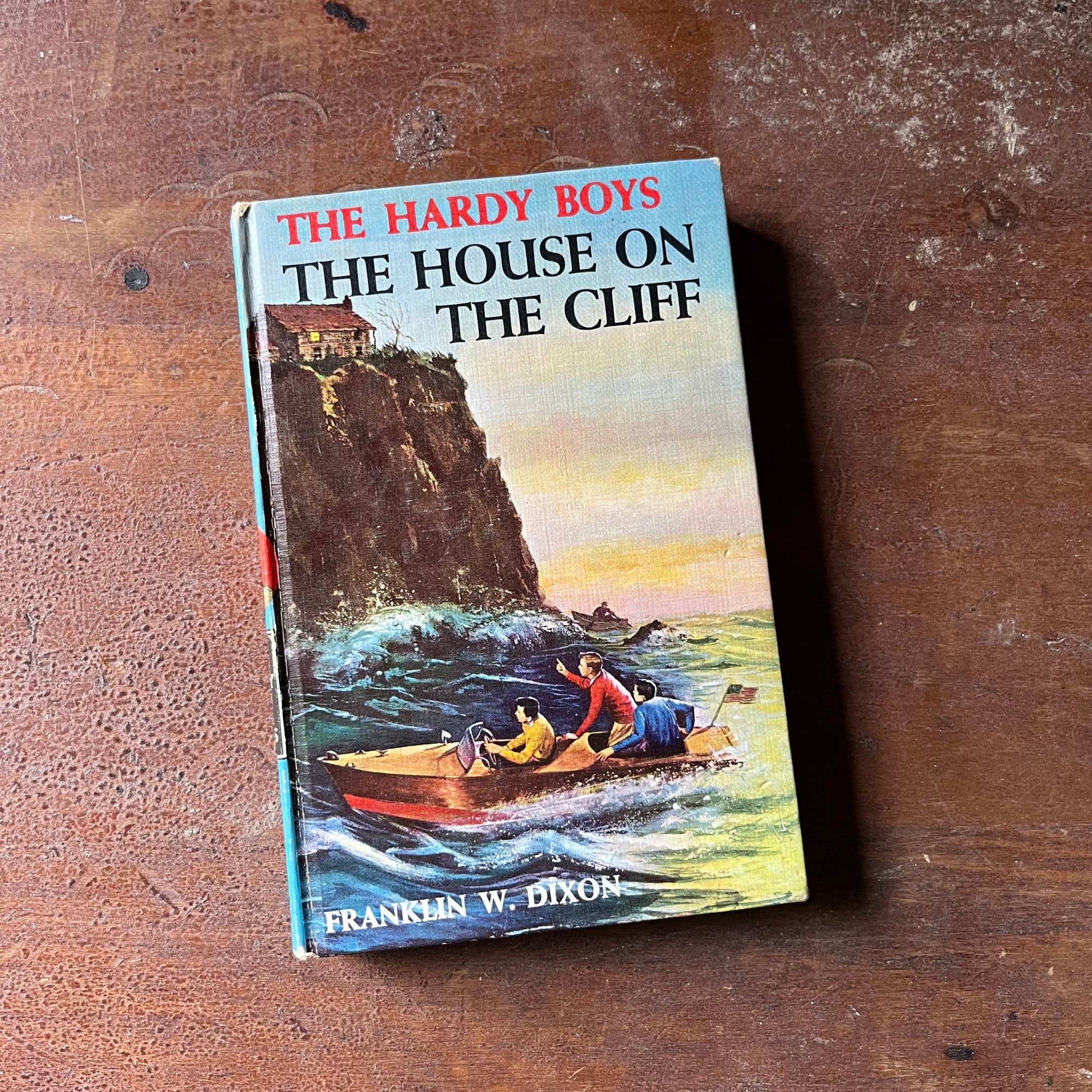 vintage children's chapter book, vintage adventure book for boys, The Hardy Boys Mystery Series Book - The Hardy Boys #2:  The House on the Cliff written by Franklin W. Dixon - view of the front cover with the boys in a boat looking up at the house on the cliff