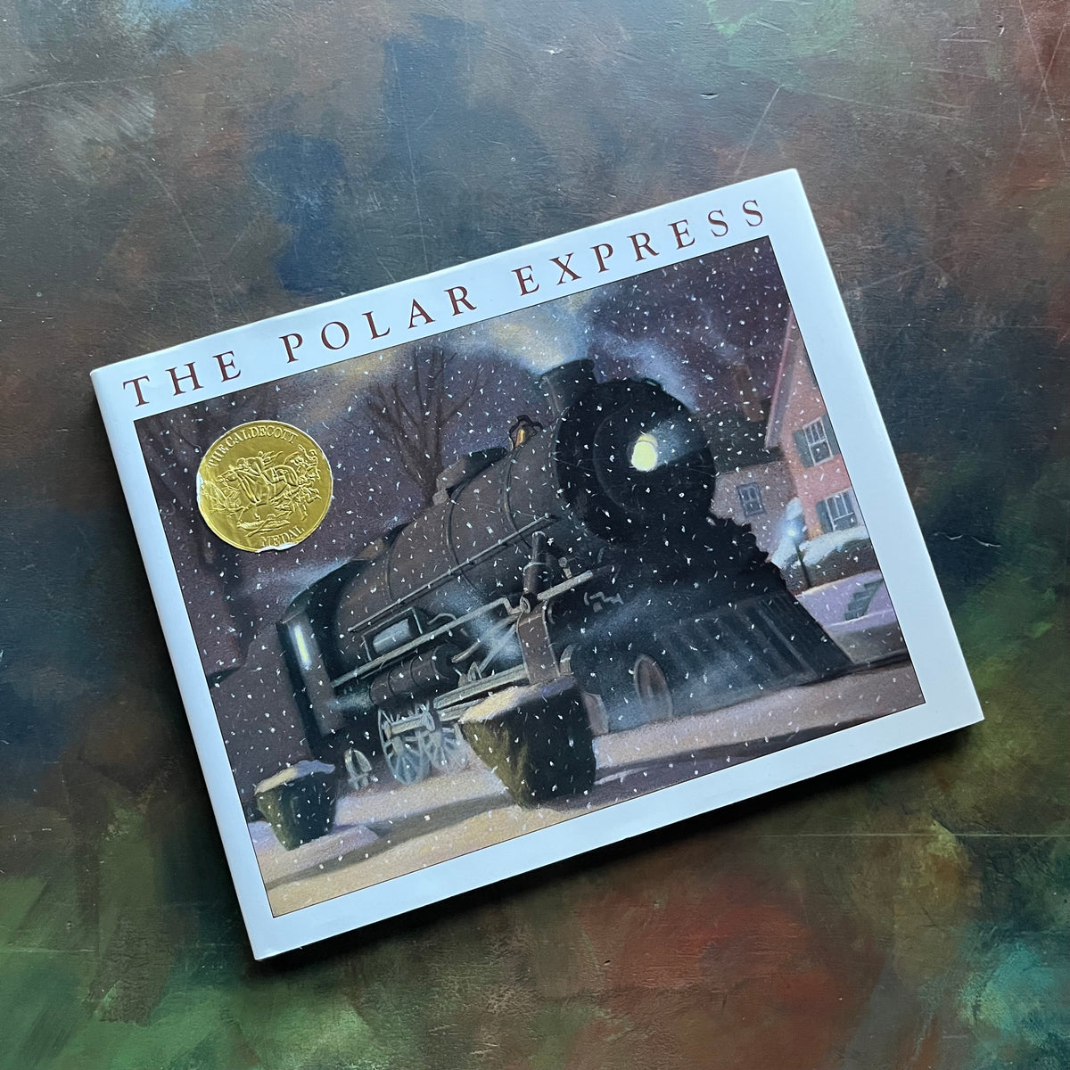 The Polar Express written and illustrated by Chris Van Allsburg-Caldecott award winning picture book-Christmas classic-view of the dust jacket's front cover with the train depicted in a neighborhood and the Caldecott Medal Seal on the cover