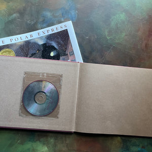 The Polar Express written and illustrated by Chris Van Allsburg-Caldecott award winning picture book-Christmas classic-view of the inside cover showing the cd tucked into a plastic sleeve against a brown background