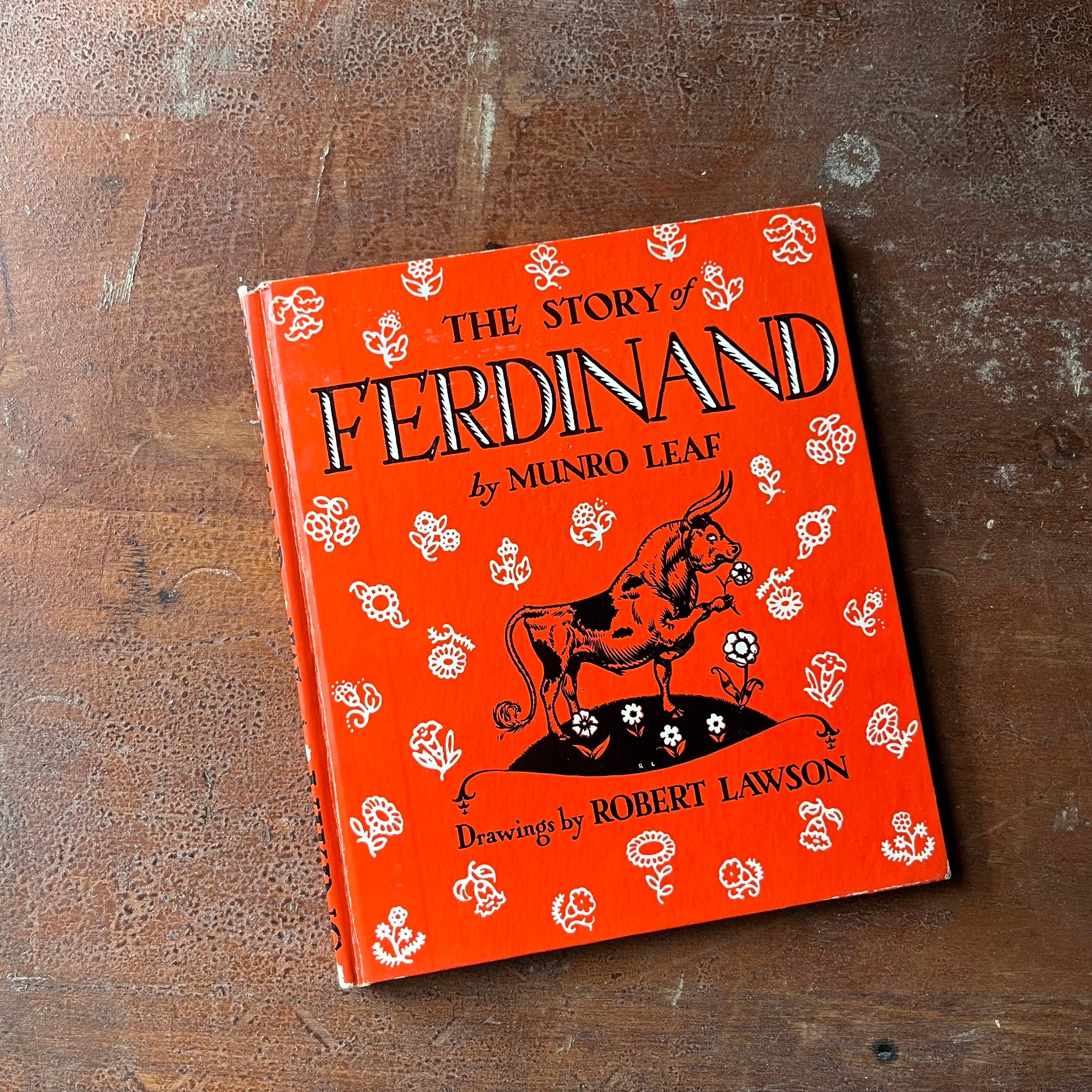 vintage children's picture book - The Story of Ferdinand written by Munro Leaf with illustrations by Robert Lawson - a 1964 Book Club Edition - view of the glossy front cover in red with flowers & Ferdinand illustrated on it along with title, author & illustrator
