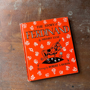 vintage children's picture book - The Story of Ferdinand written by Munro Leaf with illustrations by Robert Lawson - a 1964 Book Club Edition - view of the glossy front cover in red with flowers & Ferdinand illustrated on it along with title, author & illustrator