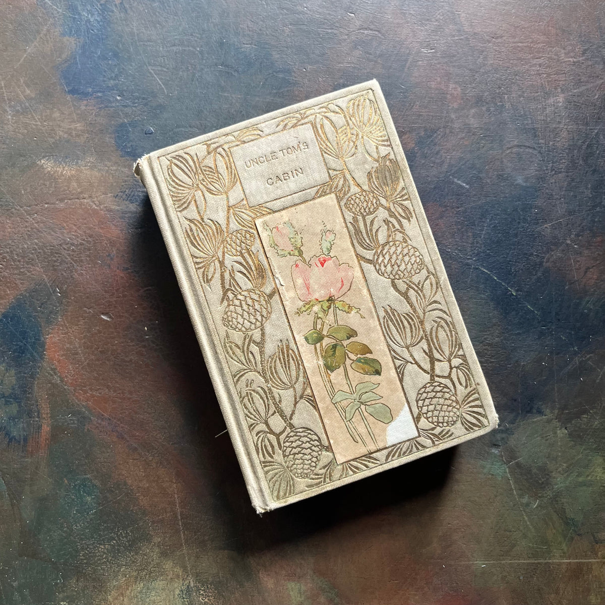 Uncle Tom’s Cabin written by Harriet Beecher Stowe-1907 Henry Altemus Petit Trianon Edition-classic American Literature-view of the front cover with embossed design with a floral print in the middle - note there is a small chunk of the floral print missing at the bottom right hand corner