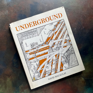 A hardcover art book titled 'UNDERGROUND' by David Macaulay, featuring a black and white architectural illustration with orange accents on the cover, photographed on a dark textured surface.