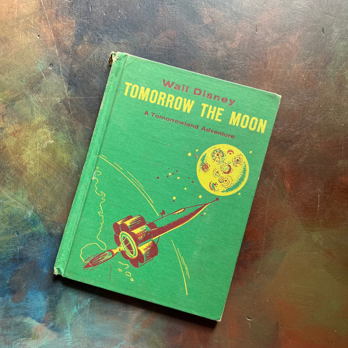 Vintage Green book titled 'Tomorrow the Moon' by Walt Disney on a textured surface-A Tomorrowland Adventure Book-Walt Disney Productions-living science book for kids-view of the front cover