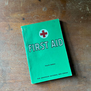 The American Red Cross First Aid Textbook 4th Edition - front cover shown sitting on a wood table