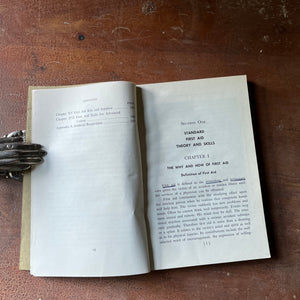 The American Red Cross First Aid Textbook 4th Edition - book opened to the copyright page & chapter one shown sitting on a wood table