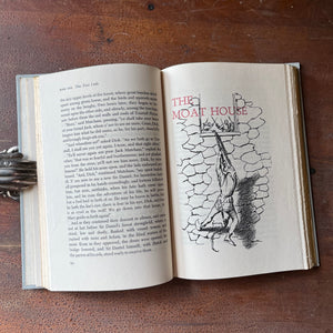The Black Arrow a 1954 Junior Deluxe Editions Children's Chapter Book sits atop a wood table with a full-page illustration shown