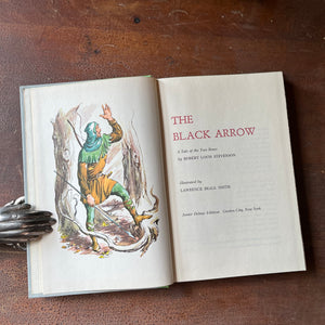 The Black Arrow a 1954 Junior Deluxe Editions Children's Chapter Book sits atop a wood table with the title page shown