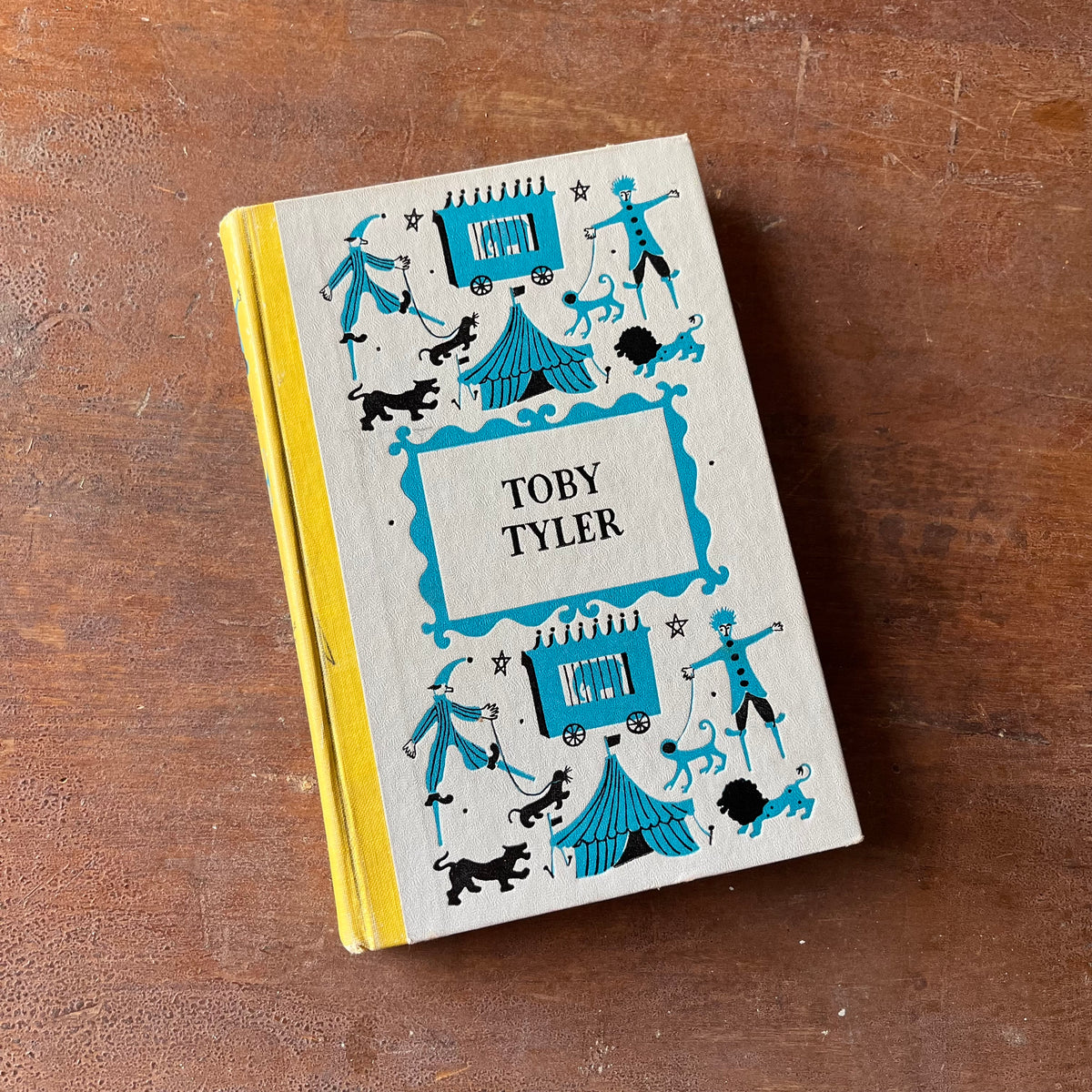 Log Cabin Vintage - vintage children's book, children's book, chapter book, Junior Deluxe Editions Book - Toby Tyler by James Otis with illustrations by Leonard Weisgard - 1958 Edition - view of the embossed front cover sitting on a wood table