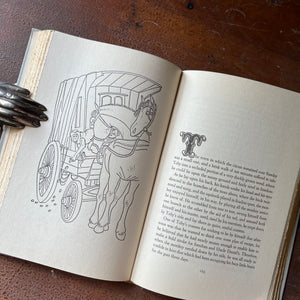 Toby Tyler by James Otis - A 1958 Junior Deluxe Editions Children's Chapter Book - shown sitting on a wood table with the book open to a full-page illustration of a horse and cart with a monkey dropping stones or nuts from the cartLog Cabin Vintage - vintage children's book, children's book, chapter book, Junior Deluxe Editions Book - Toby Tyler by James Otis with illustrations by Leonard Weisgard - 1958 Edition - view of the book sitting open to a full-page illustration  sitting on a wood table