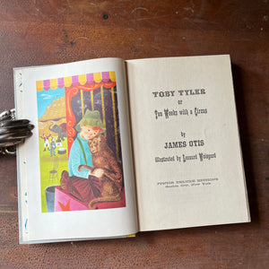 Log Cabin Vintage - vintage children's book, children's book, chapter book, Junior Deluxe Editions Book - Toby Tyler by James Otis with illustrations by Leonard Weisgard - 1958 Edition - shown sitting on a wood table with the book open to the title page