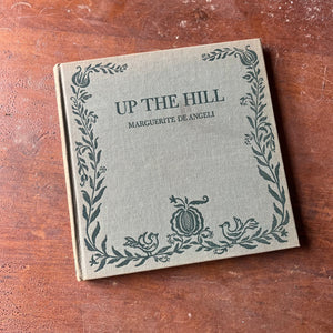 Log Cabin Vintage – vintage children’s book, children’s book, chapter book - Up the hill by Marguerite de Angeli 1942 Edition - view of the book sitting on a wood tabletop with the front cover showing