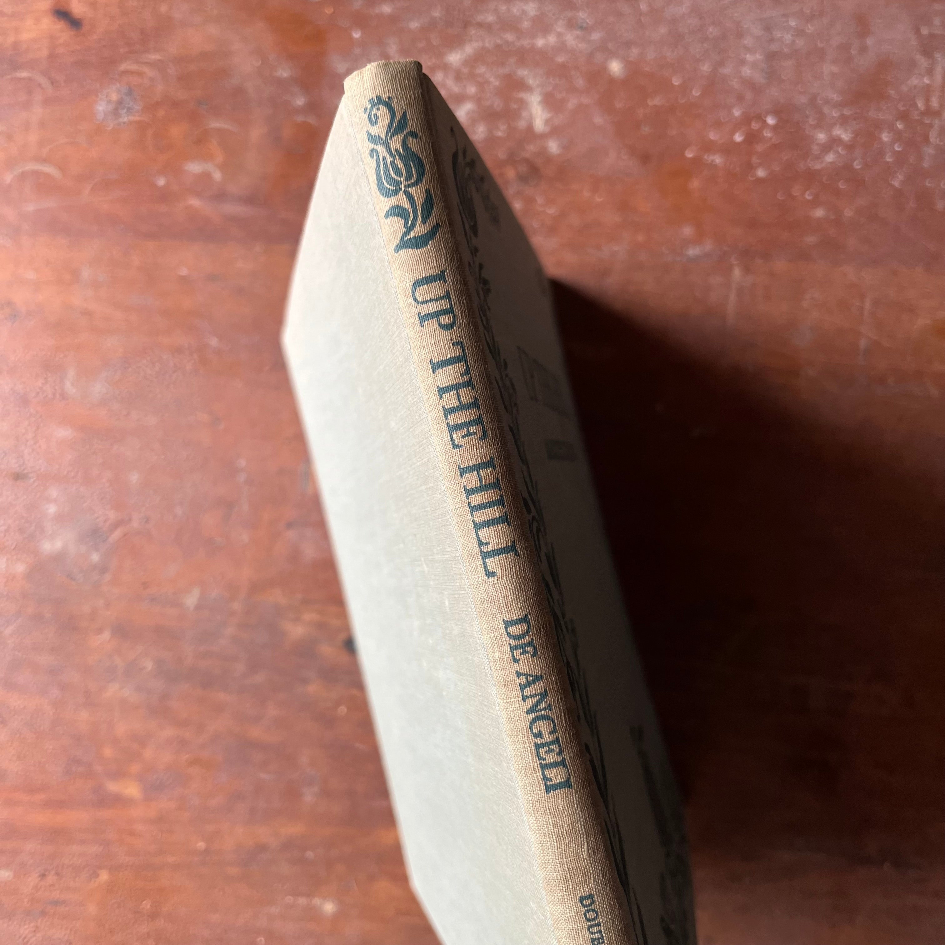 Log Cabin Vintage – vintage children’s book, children’s book, chapter book - Up the hill by Marguerite de Angeli 1942 Edition - view of the book sitting on a wood tabletop with the spine showing